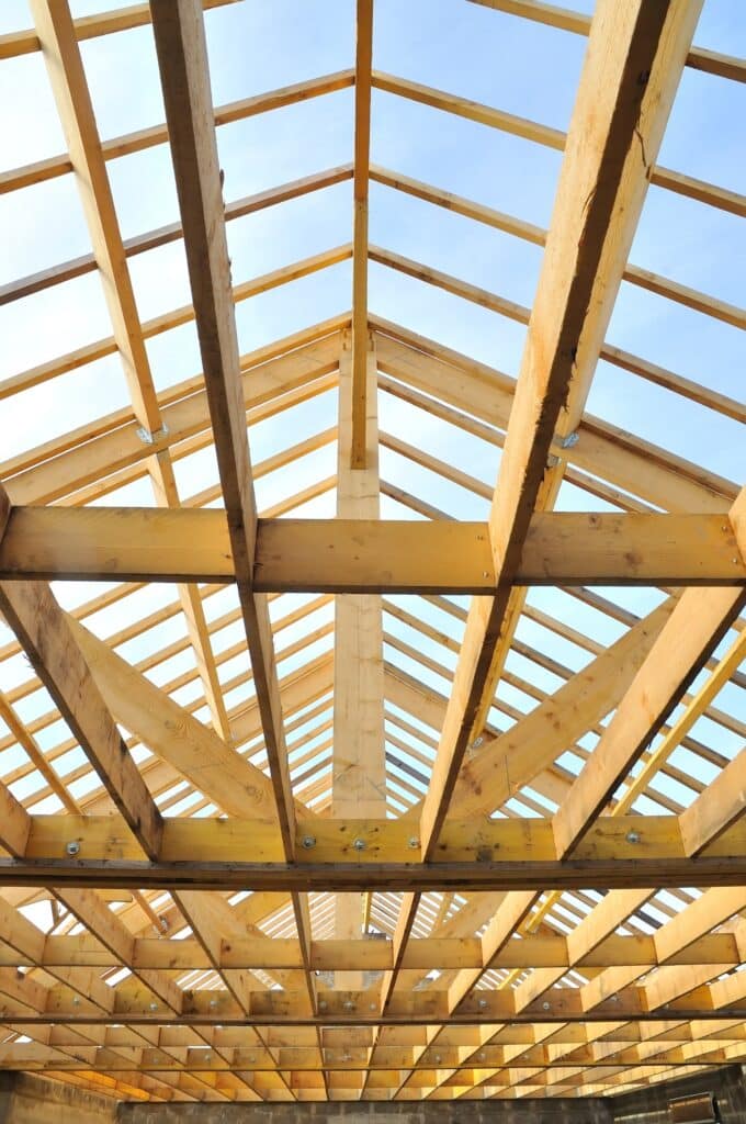 Charpente en bois : ossature et construction du toit. Charpente de toit en bois neuve vue d'en bas. Poutres maîtresses et chevrons formant une structure triangulaire sous un ciel bleu clair.